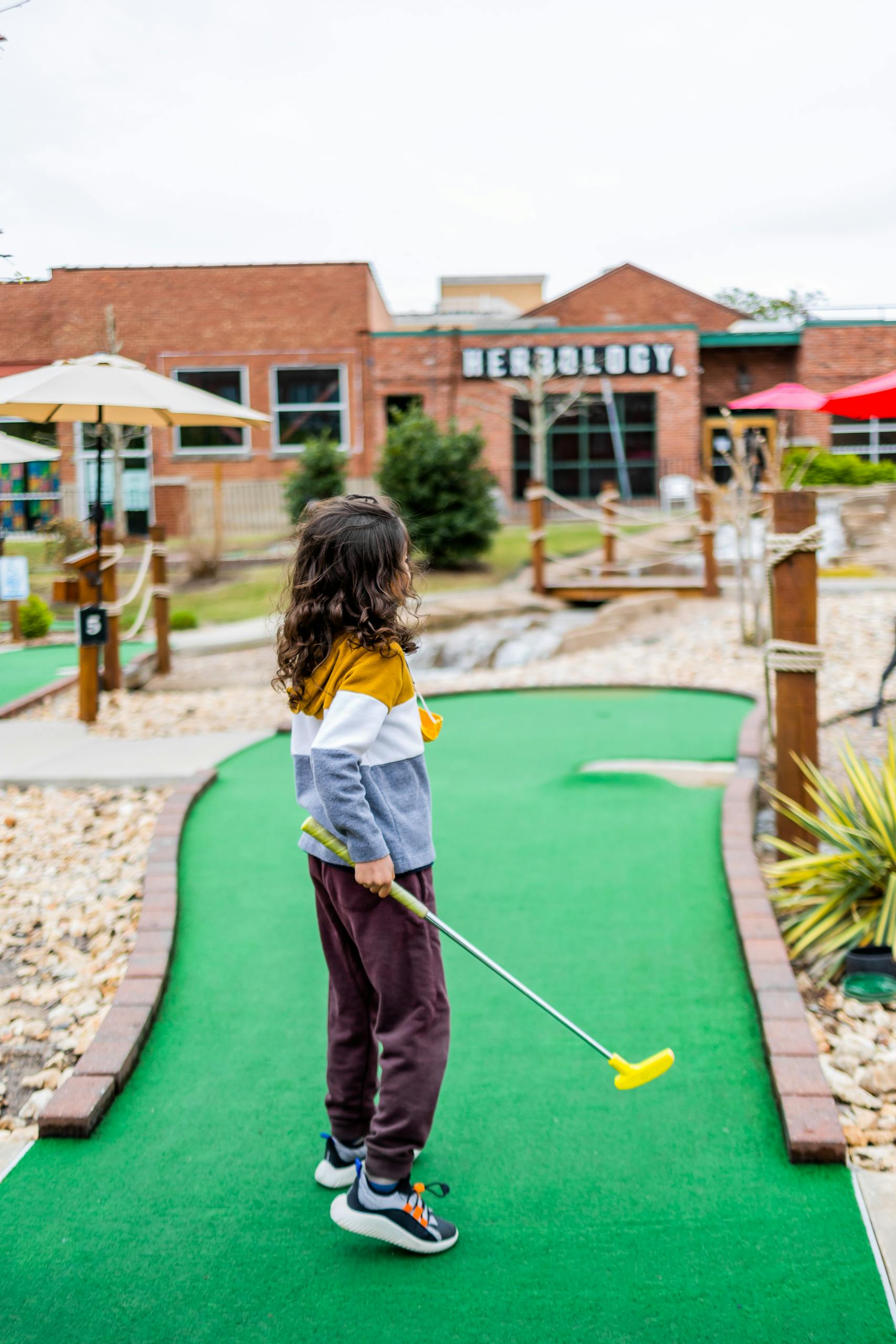 A child with long hair playing mini golf on a vibrant outdoor course. Fun and leisure.